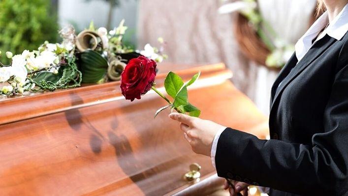 Mão depositando rosa vermelha sobre caixão – Cerimónia fúnebre com respeito, dignidade e homenagem final.
