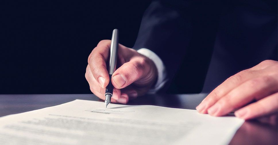 essoa a assinar documentos oficiais, ilustrando recolha de certidões e legalização de documentação funerária em Sintra, Cascais, Oeiras, Amadora e Loures.