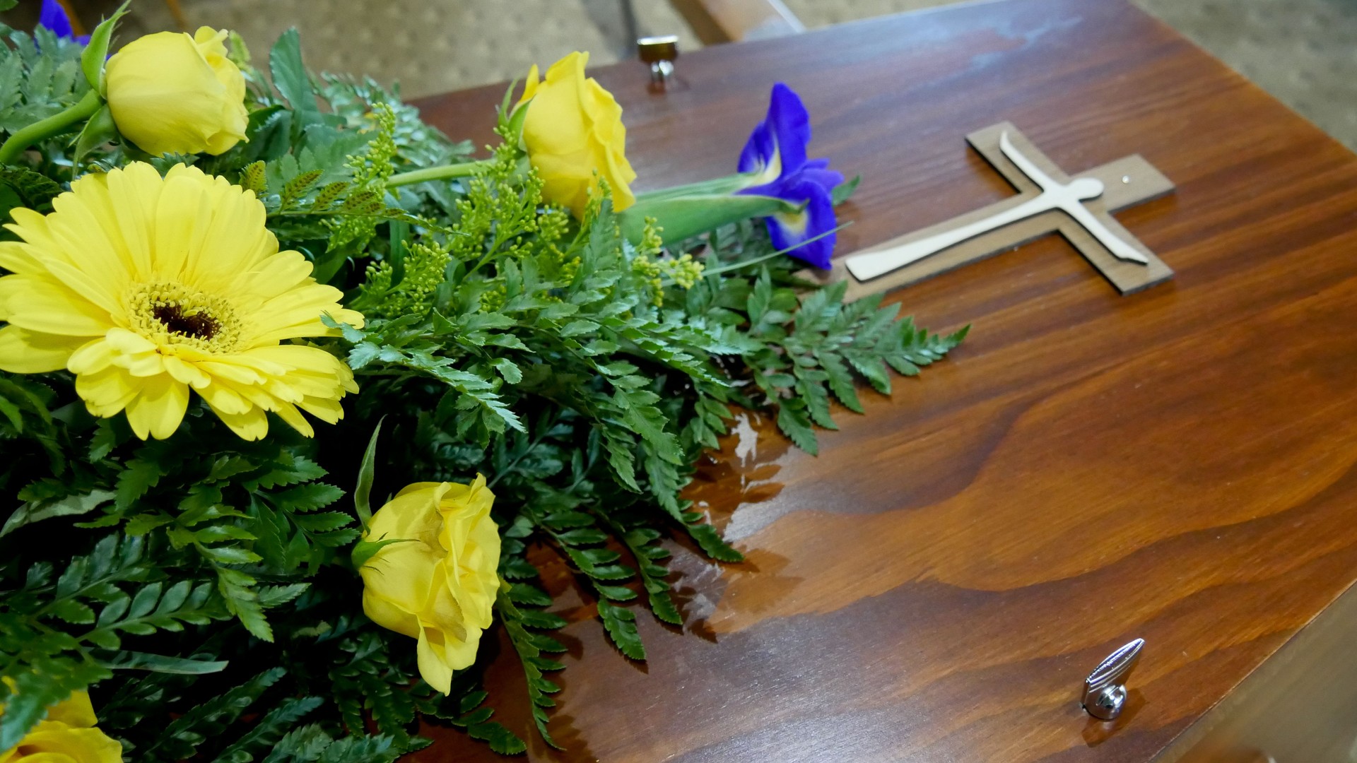 Arranjo floral amarelo sobre caixão com cruz, representando preparação e planeamento de cerimónia fúnebre pela Além Fúnebre em Sintra, Cascais, Oeiras, Amadora e Loures.