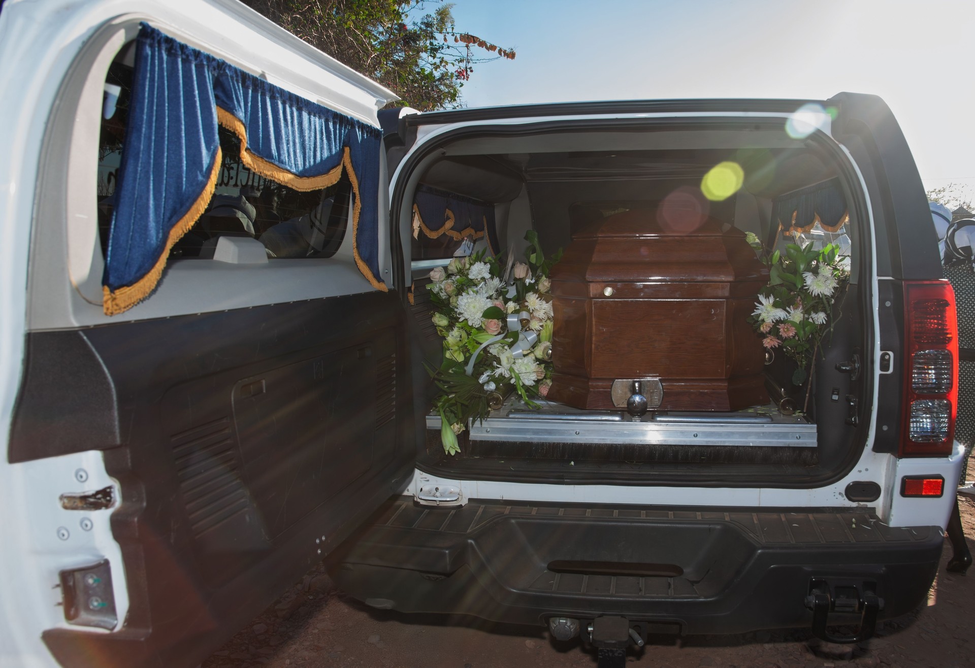 Caixão com flores a ser colocado numa viatura funerária, ilustrando serviço de logística e transporte nacional e internacional realizado em Sintra, Cascais, Oeiras e Amadora.